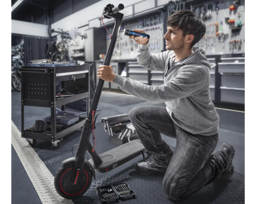 Mann repariert einen Elektroroller mit Werkzeug und einer Lampe in einer Werkstatt.