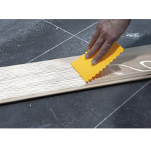 Une personne applique de la colle à l''aide d''une spatule sur une planche de bois.