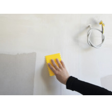 Main tenant un outil jaune pour lisser un mur.