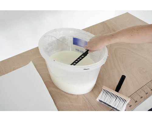 Tapetenkleister wird in einem Eimer mit einem Rührwerk gemischt, daneben liegen eine Tapetenbürste und eine Tapete.