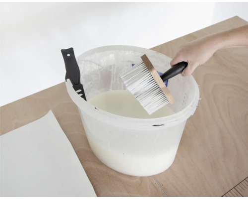Tapetenkleister im Eimer mit Quast und Tapetenmesser