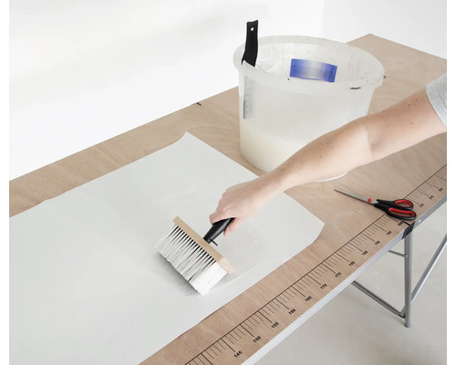 Auftragen von Kleister auf eine Tapete mit einem Quast