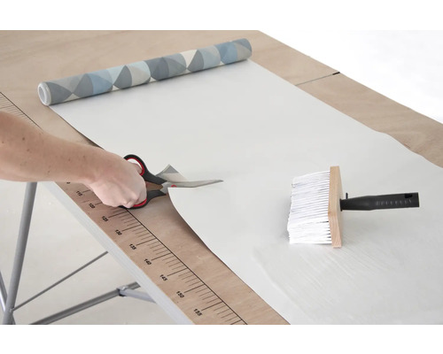 Zuschneiden von Tapete mit Schere auf einem Tapeziertisch