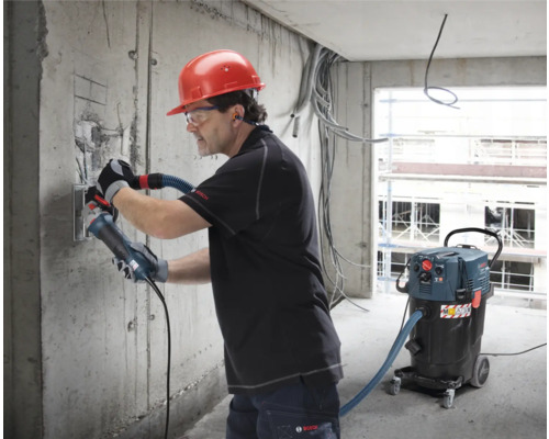 Artisan avec rainureuse à murs et aspirateur travaillant sur un mur en béton sur un chantier