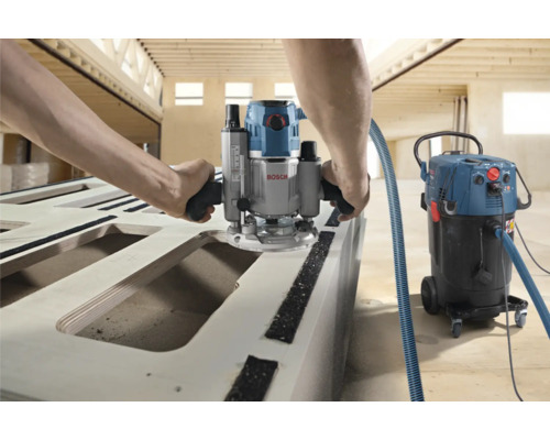 Une personne fraise du bois avec une défonceuse de la marque Bosch et un aspirateur