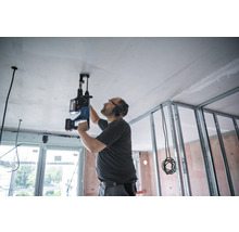 Un homme perce le plafond d''une pièce en rénovation avec un perforateur.