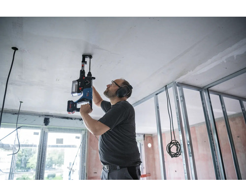 Un homme perce le plafond d''une pièce en rénovation avec un perforateur.