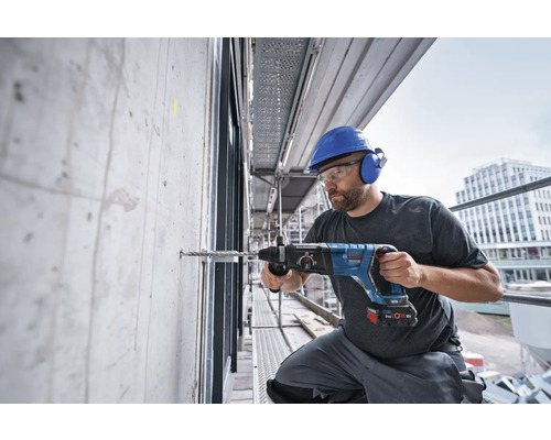 Un ouvrier perce un trou dans un mur en béton avec un perforateur sur un échafaudage.