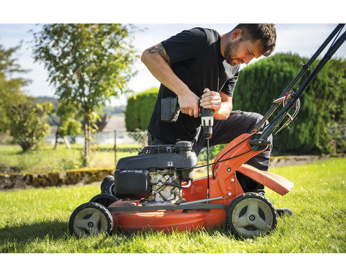 Mann repariert Rasenmäher mit Akkuschrauber im Garten.