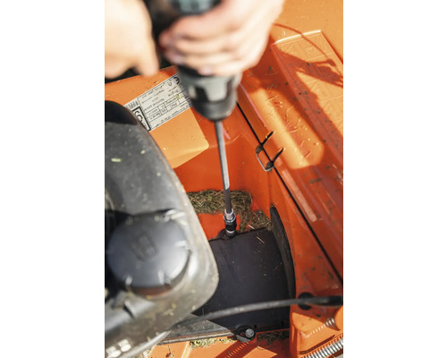 Eine Person benutzt einen Schraubendreher, um einen Rasenmäher zu reparieren.