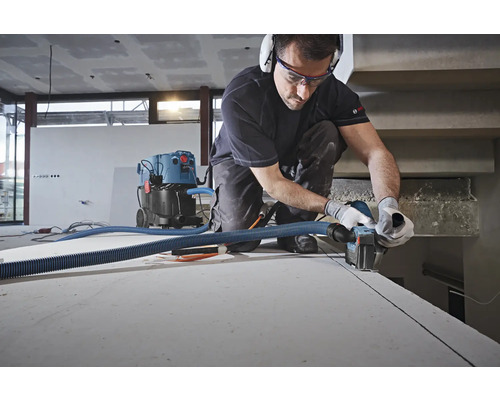 Un artisan découpe un joint dans un mur à l''aide d''une rainureuse à murs, un aspirateur est branché.