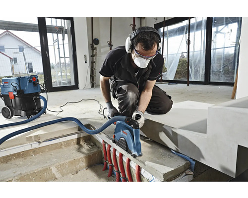 Un homme travaille avec une rainureuse à murs et un aspirateur dans une pièce.