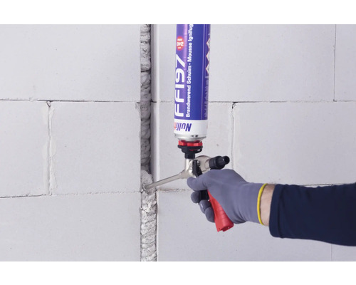 Handwerker füllt mit einem Pistolenschaum eine Fuge in einer Wand aus Porenbeton.