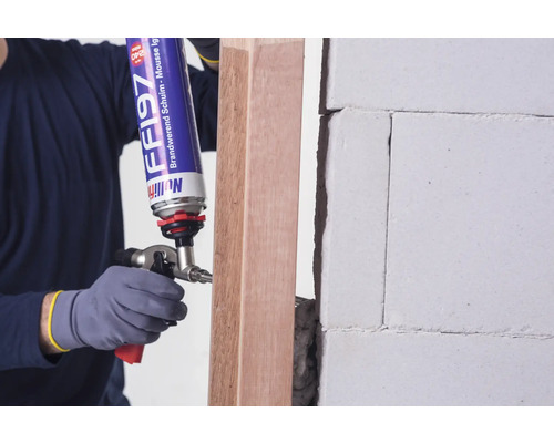 Handwerker verwendet Brandschutzschaum zur Abdichtung eines Holzrahmens an einer Wand.