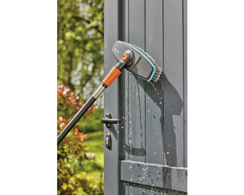 Brosse de lavage Gardena avec manche télescopique nettoyant une porte de jardin