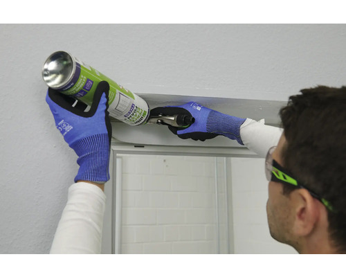 Une personne portant des lunettes de protection et des gants utilise de la mousse de construction pour installer une cabine de douche.