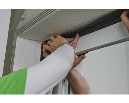 Eine Person befestigt Dichtungsband an einem Türrahmen.