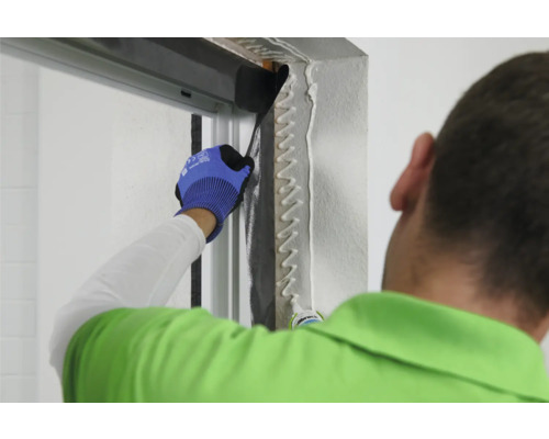 Une personne applique du produit d''étanchéité sur un cadre de porte pour garantir une fermeture hermétique.