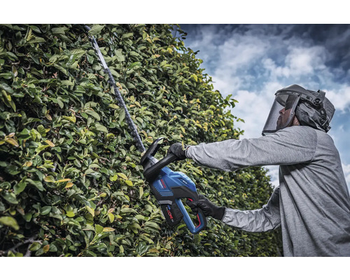 Mann mit Schutzvisier schneidet Hecke mit Akku-Heckenschere