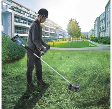 Eine Person benutzt einen Rasentrimmer mit Akku in einem Wohngebiet, um Gras zu schneiden.