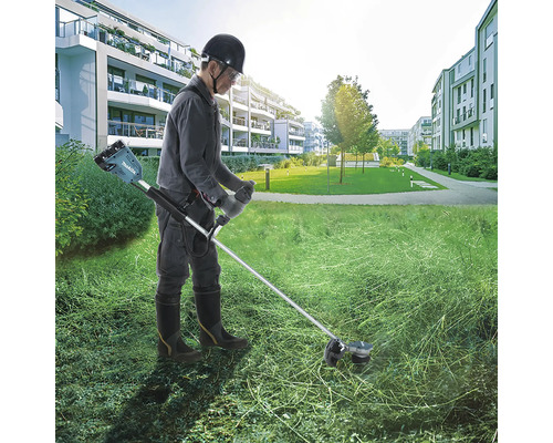 Eine Person benutzt einen Rasentrimmer mit Akku in einem Wohngebiet, um Gras zu schneiden.