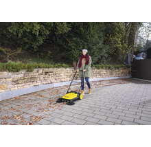 Une femme utilise une balayeuse jaune à l''extérieur pour nettoyer les feuilles sur les pavés.