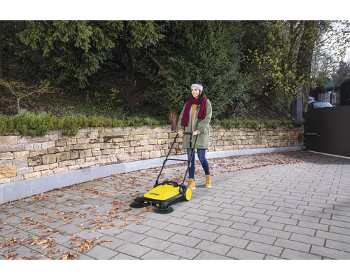 Une femme utilise une balayeuse jaune à l''extérieur pour nettoyer les feuilles sur les pavés.