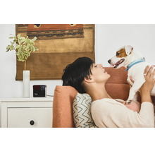 Femme se détend avec un chien et une caméra de surveillance Petcube sur le canapé