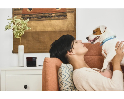 Femme se détend avec un chien et une caméra de surveillance Petcube sur le canapé