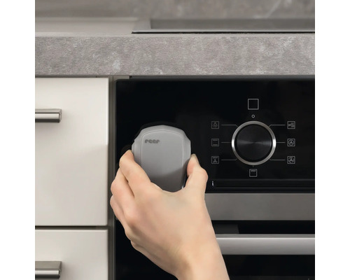 Une main fixe une sécurité de cuisinière Reer sur une cuisinière.