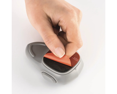 Une main retire le film protecteur d''un crochet adhésif.