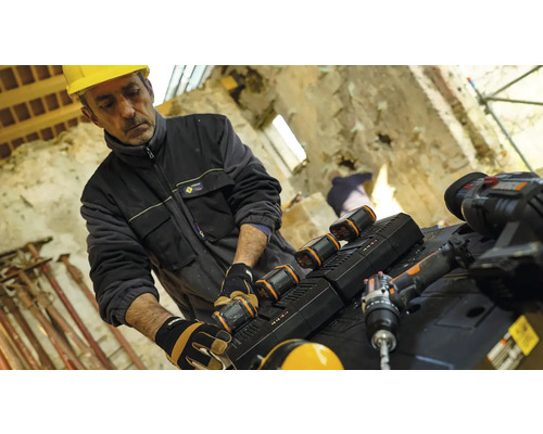 Un ouvrier du bâtiment portant un casque de sécurité change la batterie d''un outil électrique sur un chantier.