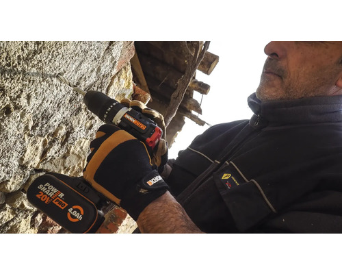 Un homme perce un trou dans un mur de pierre avec une perceuse sans fil.