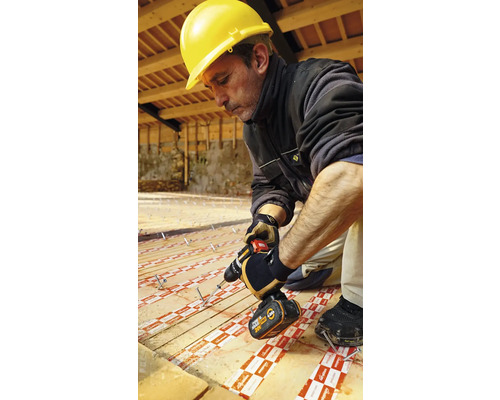 Artisan avec casque de protection et visseuse sans fil installant des panneaux isolants sur un plancher en bois.
