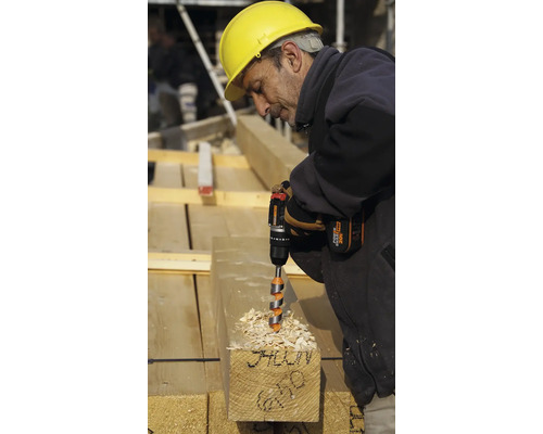 Un ouvrier du bâtiment perce une poutre en bois avec une perceuse sans fil.