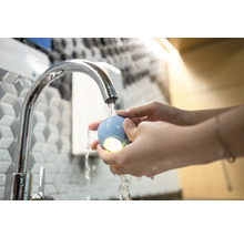 Szene einer Person, die unter einem Wasserhahn einen leuchtenden, runden Gegenstand hält