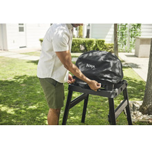 Mann befestigt Schutzhülle auf Ninja Grill im Garten.