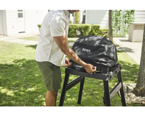 Mann befestigt Schutzhülle auf Ninja Grill im Garten.