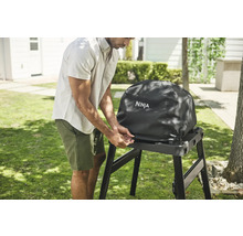 Mann befestigt eine Schutzhülle mit Ninja Logo an einem Grill