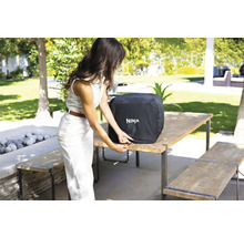 Eine Frau befestigt die Wetterschutzhülle von Ninja auf einem Grill im Freien.