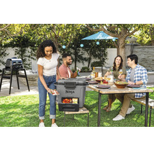 Szene im Garten mit Personen, einem Esstisch, einem Grill und einer Kühlbox der Marke Ninja