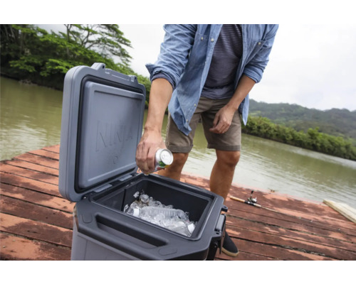 Person legt Getränkedose in Kühlbox mit Eis auf einem Holzsteg.