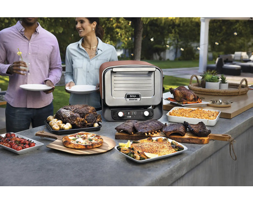 Scène avec un four d''extérieur Ninja Woodfire et divers plats préparés à l''extérieur.