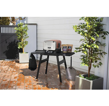 Scène d''extérieur avec un barbecue électrique Ninja Woodfire et des accessoires sur une table.