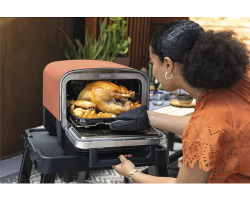 Femme ouvrant le four avec un poulet rôti