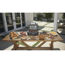 Scène extérieure avec une table remplie de plats préparés avec un gril électrique.