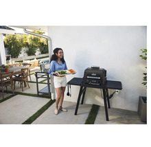 Femme avec plateau de légumes debout à côté d''un barbecue électrique à l''extérieur.