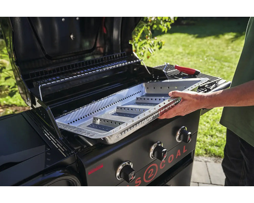 Un homme place un bac à charbon de bois dans un barbecue à gaz pour le charbon de bois