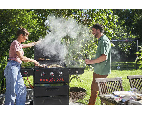 Femme et homme grillant avec un barbecue à gaz et à charbon de bois dans le jardin.