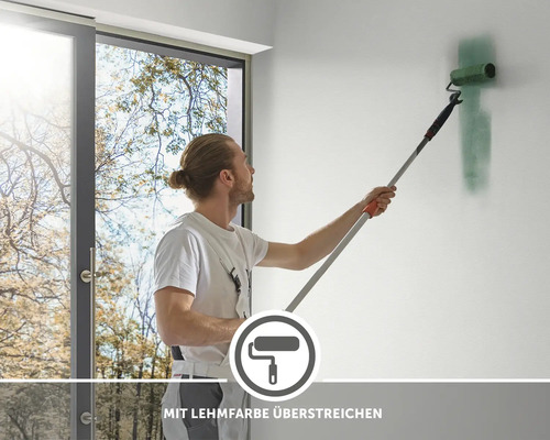 Mann streicht Wand mit Lehmfarbe und Farbroller mit Stiel